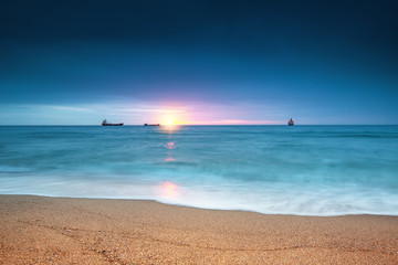 Fototapeta na wymiar Cargo ship sailing on sunrise near the beach