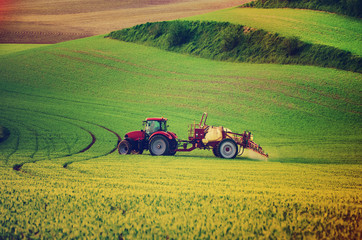 Fototapeta premium Farm machinery spraying insecticide to the green field, agricultural natural seasonal spring background, vintag retro hipster style