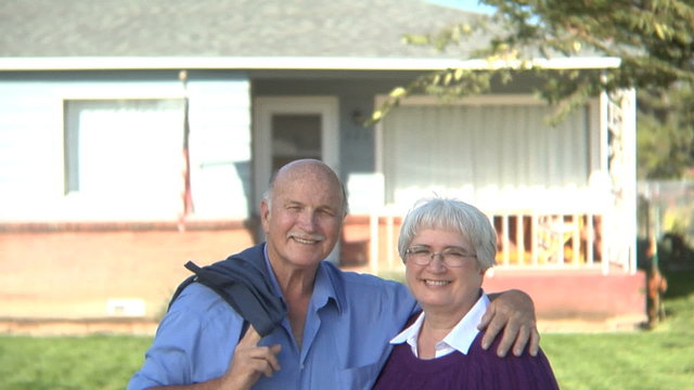 Senior couple standing in front of home smiling