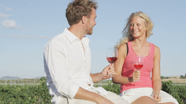Red wine drinking couple toasting at vineyard. Romantic woman and man drinking red or rose wine smiling happy doing toast. Romantic lovers outside. Young Caucasian man and woman.