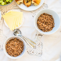 Table set for Breakfast. Buckwheat Porridge White Bowls, Cheese Slices, Pastries and Grapes