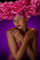 Naklejka premium Beautiful young blonde woman in big hat with pink flowers on dark blue background