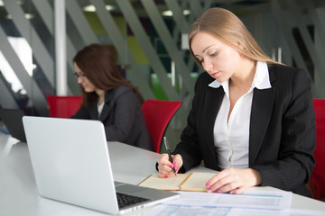 Young businesswoman sitting at workplace and reading paper in office
