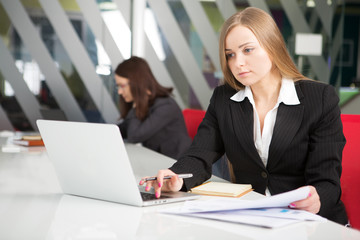 Young businesswoman sitting at workplace and reading paper in office
