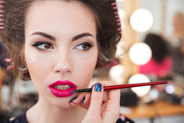 Makeup artist doing makeup and applying pink lipstick using brush