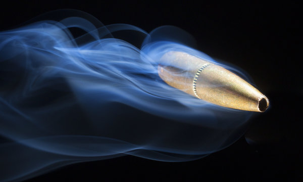 Near miss as a copper jacketed precision bullet streaks by on a black background with smoke trailing behind