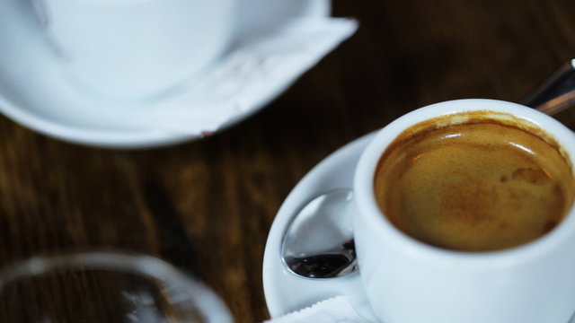 Close up of tasty coffee served in white cups, one with flower shape made of foam with sugar stickers and silver spoons on little fansy plates.