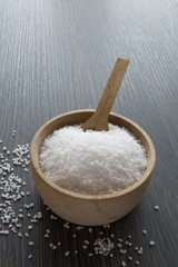 A wooden bowl of salt crystals on a wooden background