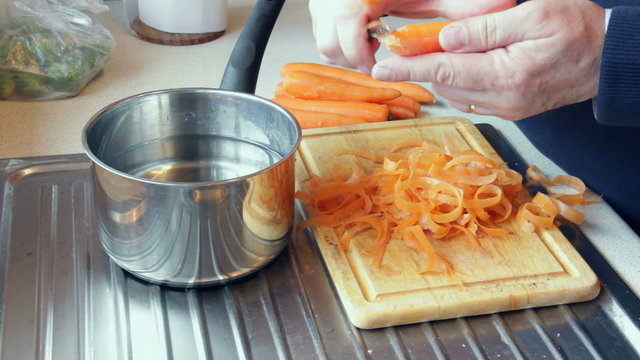 Middle-aged man in close up peeling the last of a small quantity of carrots in a domestic kitchen, prior to cooking them.