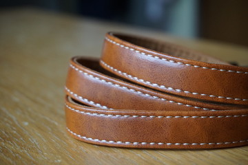 Brown leather band with white stitching on the wooden desk 