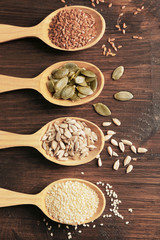 Sesame, flax, pumpkin and sunflower seeds in wooden spoons on table, closeup