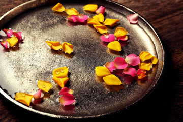 Pink and yellow rose petals in silver bowl with water on wooden background