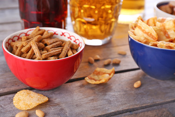 Mugs of beer and bowls with snacks on wooden table