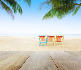 Fototapeta na wymiar wood table top on blur beach background with beach chairs under coconut tree