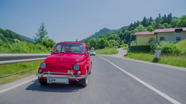 Small red vintage car passing the nearby houses