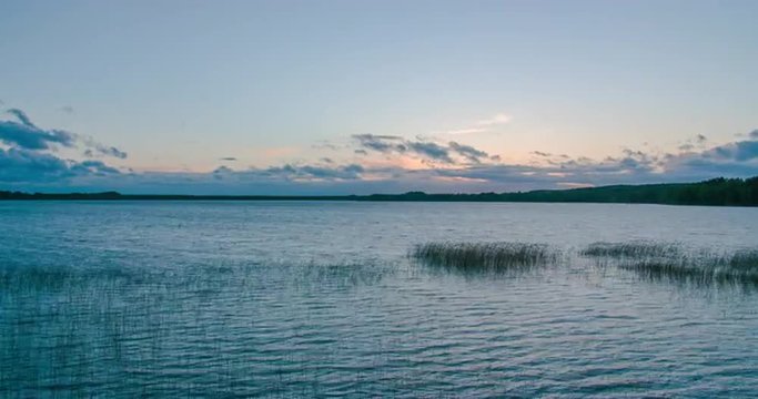Time lapse of a sunset over a large lake with forest on horizon