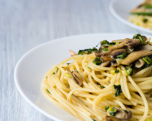 Two plates of pasta with mushrooms and green onions on a white p