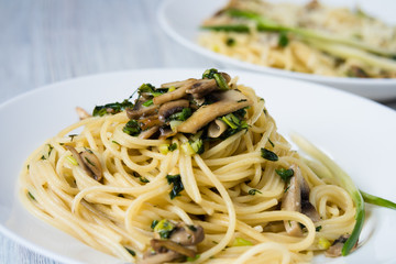 Two plates of pasta with mushrooms and green onions on a white p
