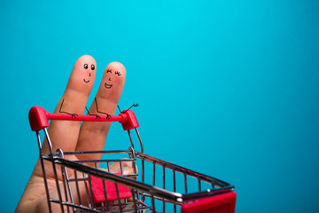 Funny fingers shopping at supermarket with red cart trolley on blue background © projectio