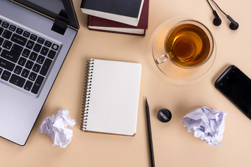 Office table desk with supplies, white blank note pad, cup, pen, pc, crumpled paper, flower on wooden background. Top view