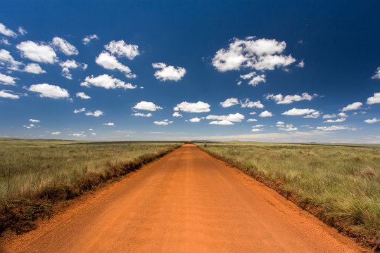 Rural orange dirt road with blue sky and far horizon