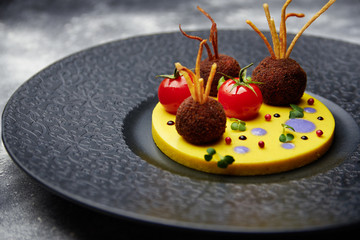 Fried meatballs with tomato on a potatoes in a black plate.