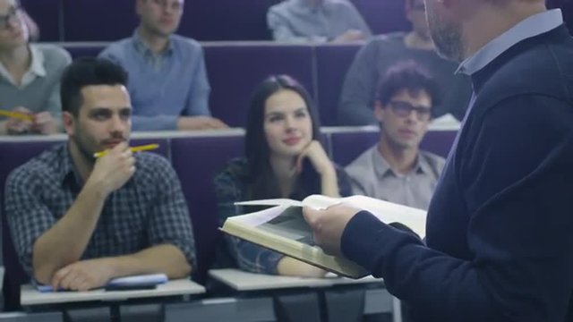 College professor is teaching a class of multi-ethnic students while holding a book. Shot on RED Cinema Camera.
