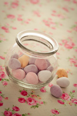 Chocolate mini eggs in a glass far. A couple of mini eggs are loose beside the jar focus is on egg in the foreground.