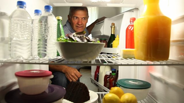 Senior man opens frig and takes salad