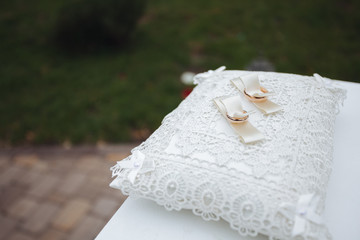 Two golden wedding rings on a white silk pillow.