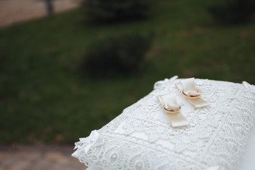 Two golden wedding rings on a white silk pillow.