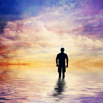 Man in water of calm ocean looking at the fairytale, fantastic sunset sky.