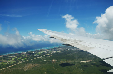 Obraz premium Wing of an airplane flying above the clouds over tropical island