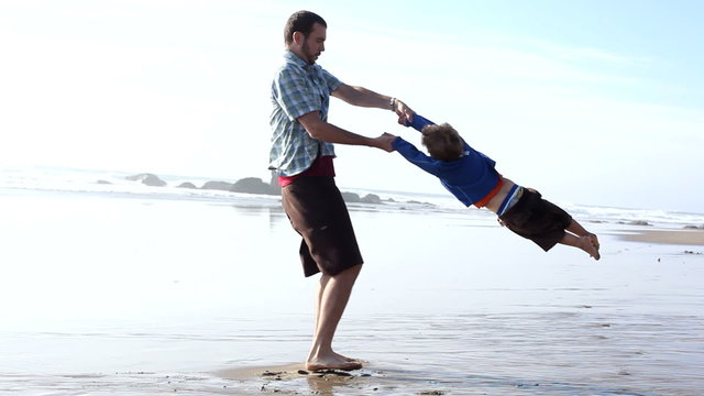 Father spinning around with son at beach