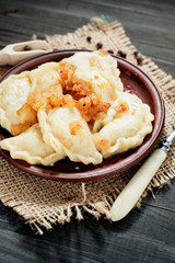 traditional Ukrainian and Russian cuisine , dumplings called varenyky of dough with cabbage, pepper and fat or salo in a clay plate on a dark wooden background