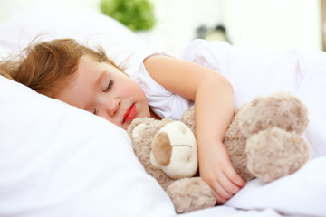 child little girl sleeps in the bed with teddy bear