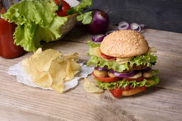 Delicious burger with beef, tomato, cheese, lettuce and potato chips on wooden counter.