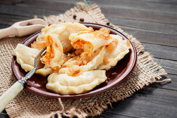 traditional Ukrainian and Russian cuisine , dumplings called varenyky of dough with cabbage, pepper and fat or salo in a clay plate on a dark wooden background