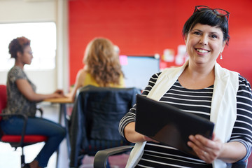 Fototapeta premium Confident female designer working on a digital tablet in red creative office space