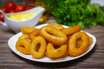 deep fried calamari with sauce and salad on a wooden background