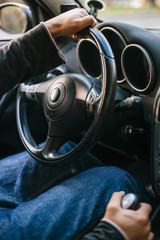 Close up of a man's hand on a steering wheel driving a car.
