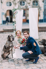 Young attractive wedding couple posing with dog giving a pow with the ancient european architecture on background 