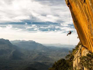 Abseiling a negative yellow rock wall with mountains on backgrou