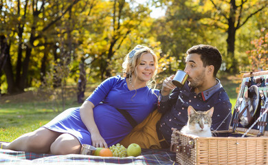 Pregnant happy and smiling couple on picnic with cat