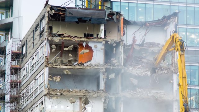Timelapse of excavator demolishing building in central London, with water spray to avoid dust. A digger with a long arm breaks concrete and bricks during destruction of a residential structure
