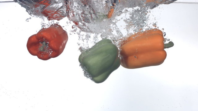 Bell peppers splashing into water, slow motion