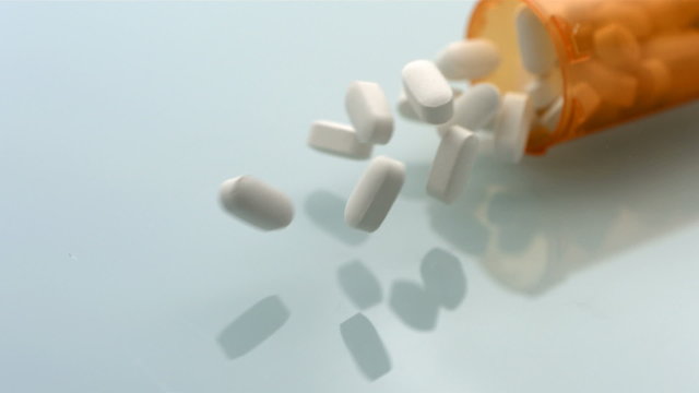 Pill bottle falling on reflective surface, slow motion