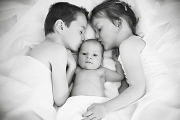 Brother and sister kissing newborn baby