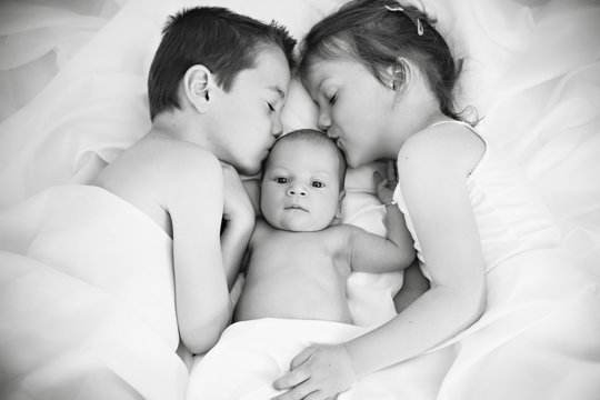 Brother And Sister Kissing Newborn Baby