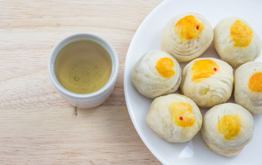 Chinese Pastry Mung Bean or Mooncake with Egg Yolk on dish wooden table and green tea cup